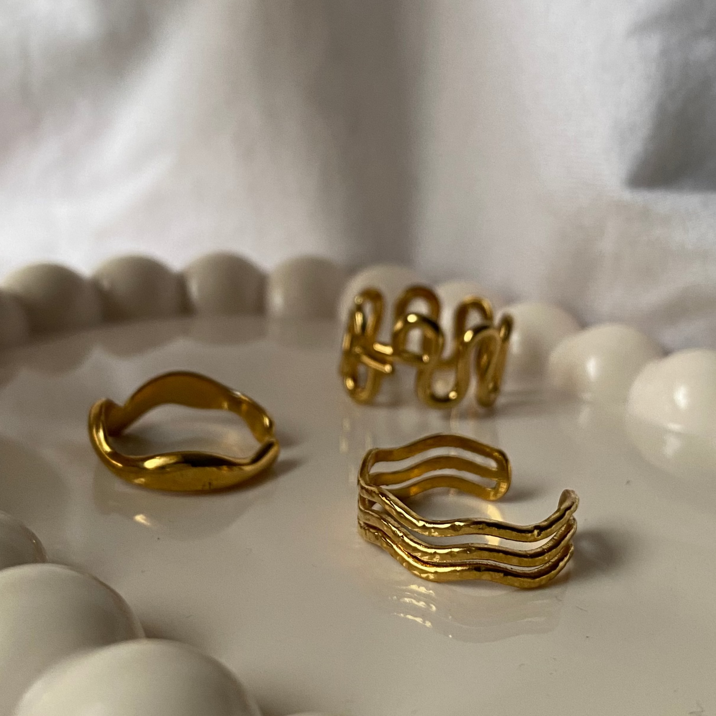 Gold rings on a white ceramic dish with a white fabric background